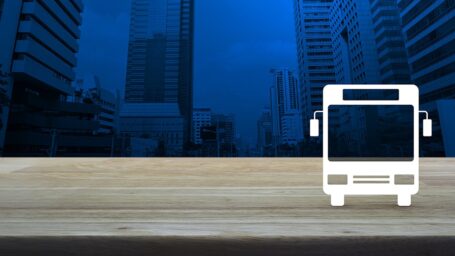 Bus flat icon on wooden table over modern office city tower, Business transportation service concept
