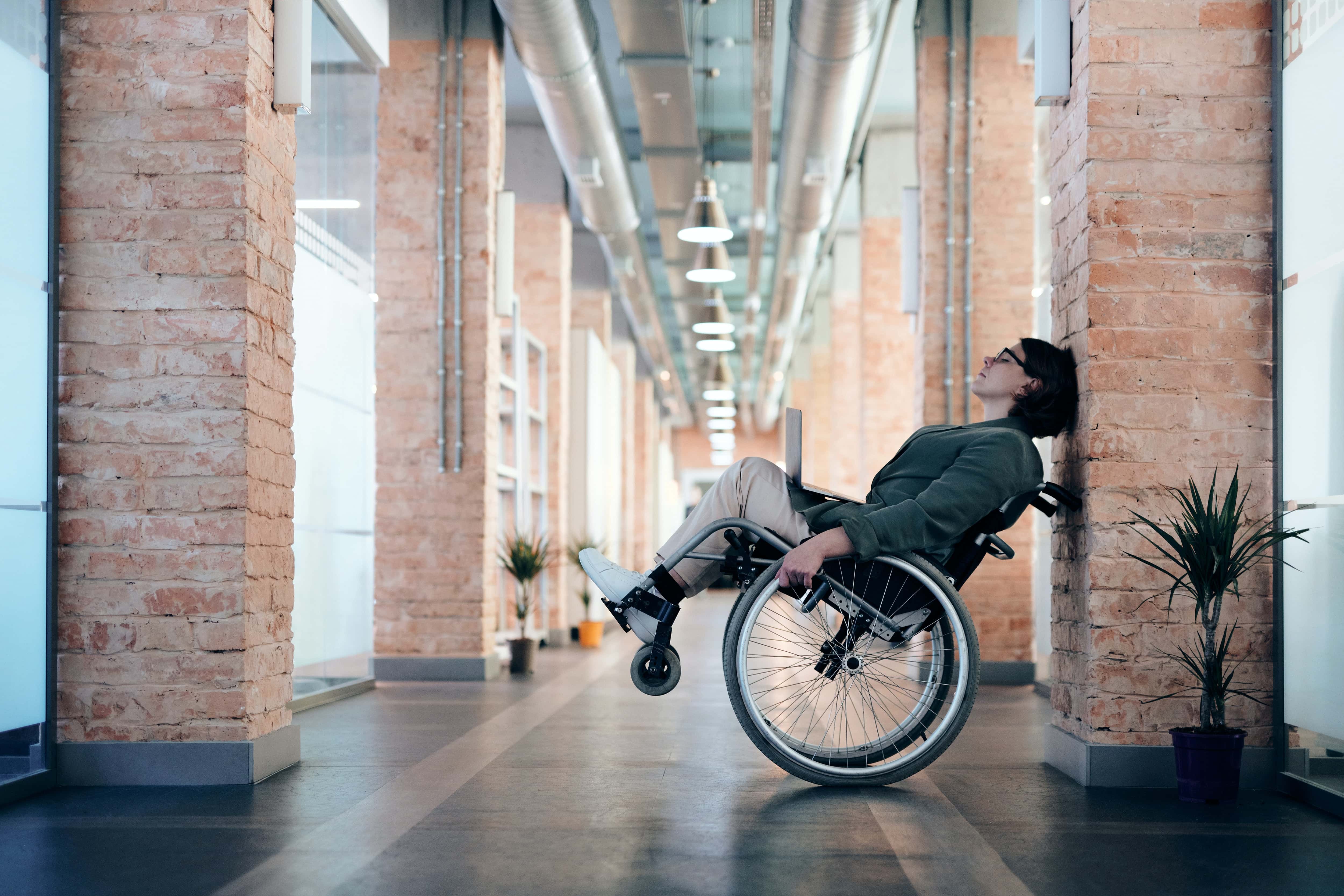 Photo of Woman Sitting on Wheelchair While Leaning on Wall