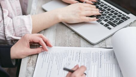 one person typing on a laptop next to another person taking notes